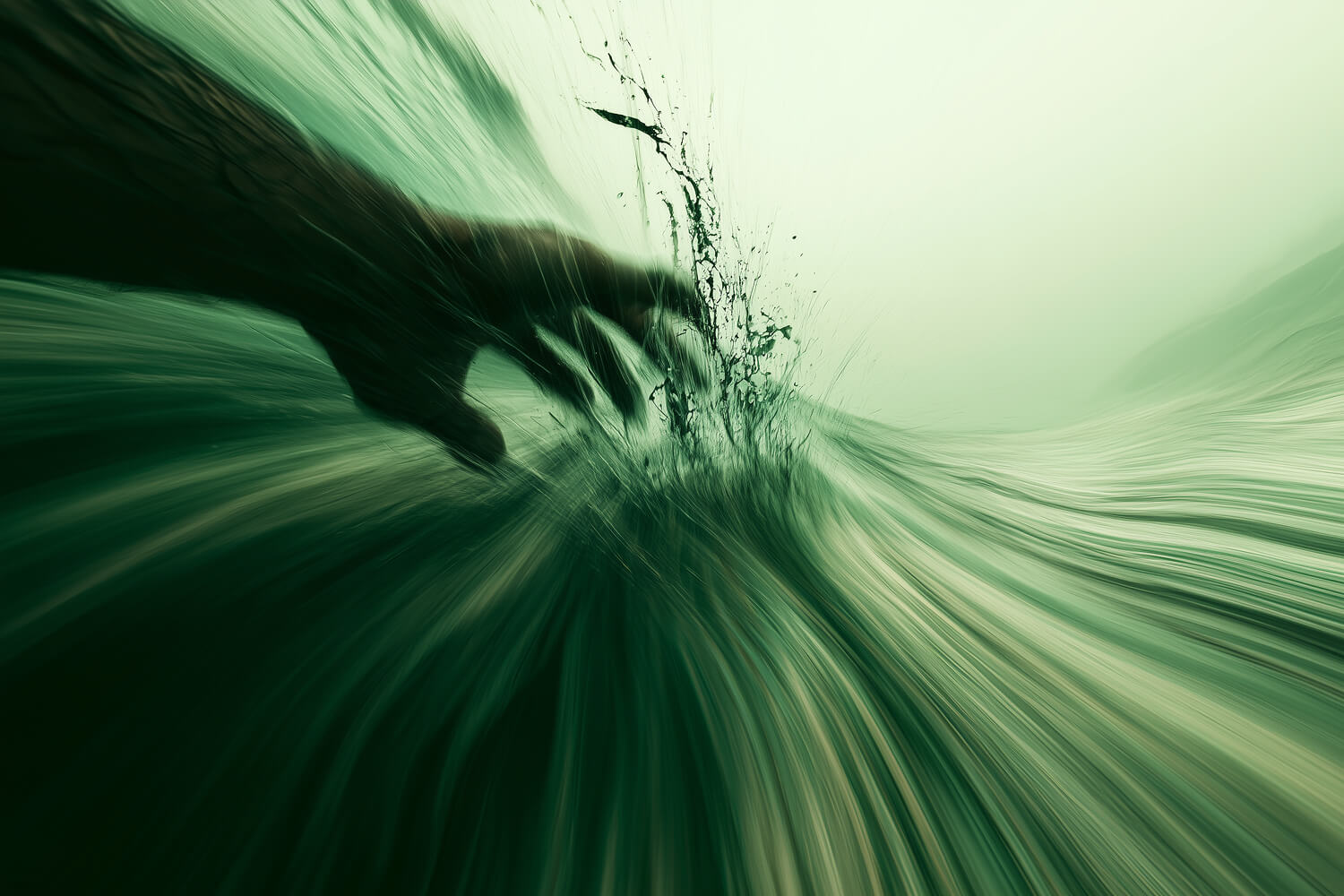 Hand trailing through a green wave, throwing up spray