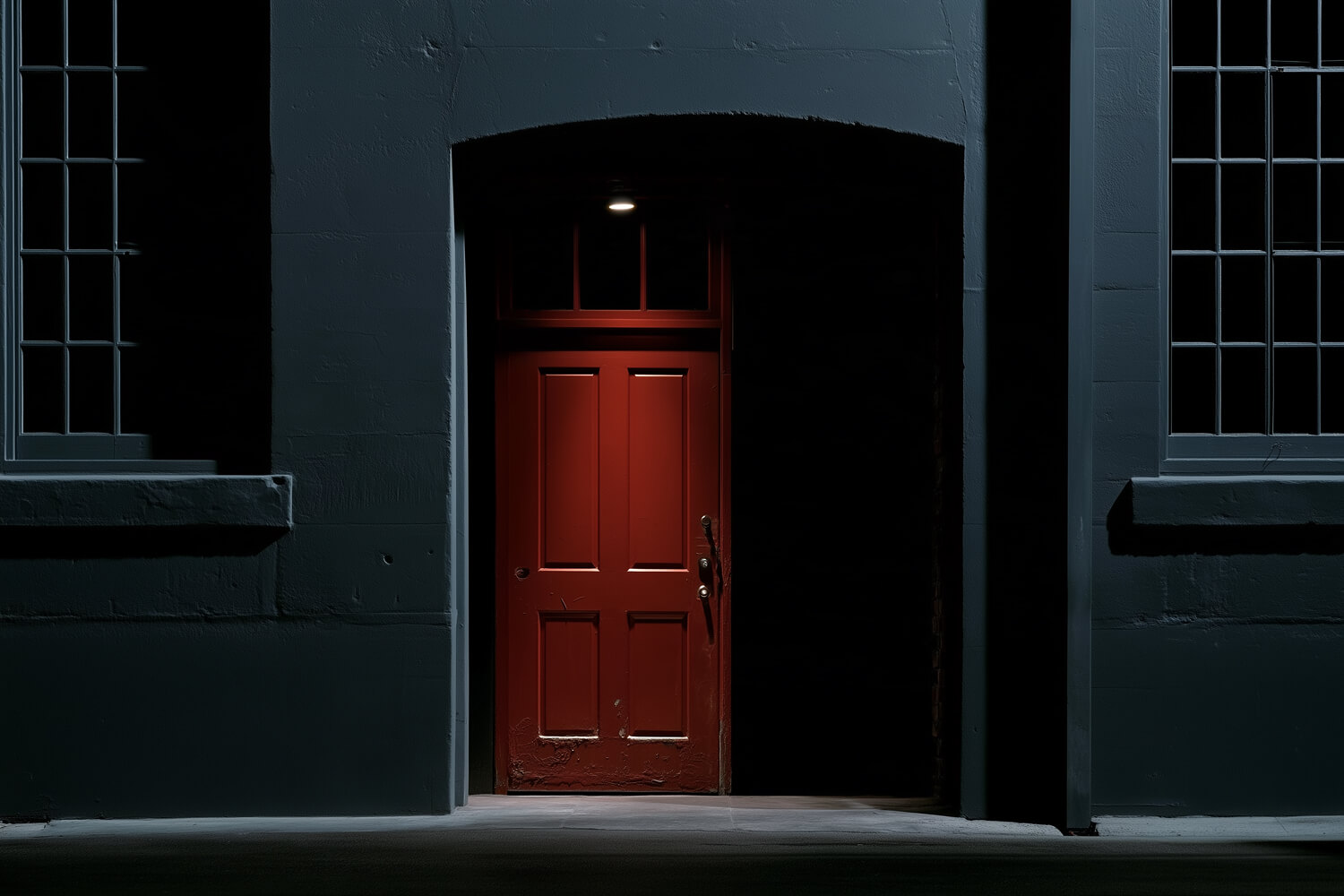 Red door glowing inside a dark grey stone archway at night