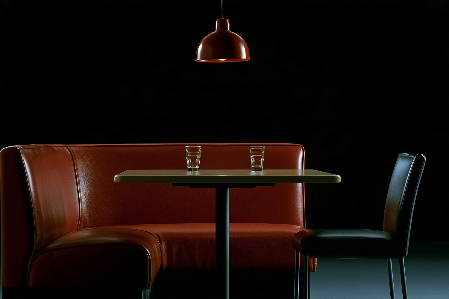 Red leather booth and table set with two glasses under a red pendant lamp