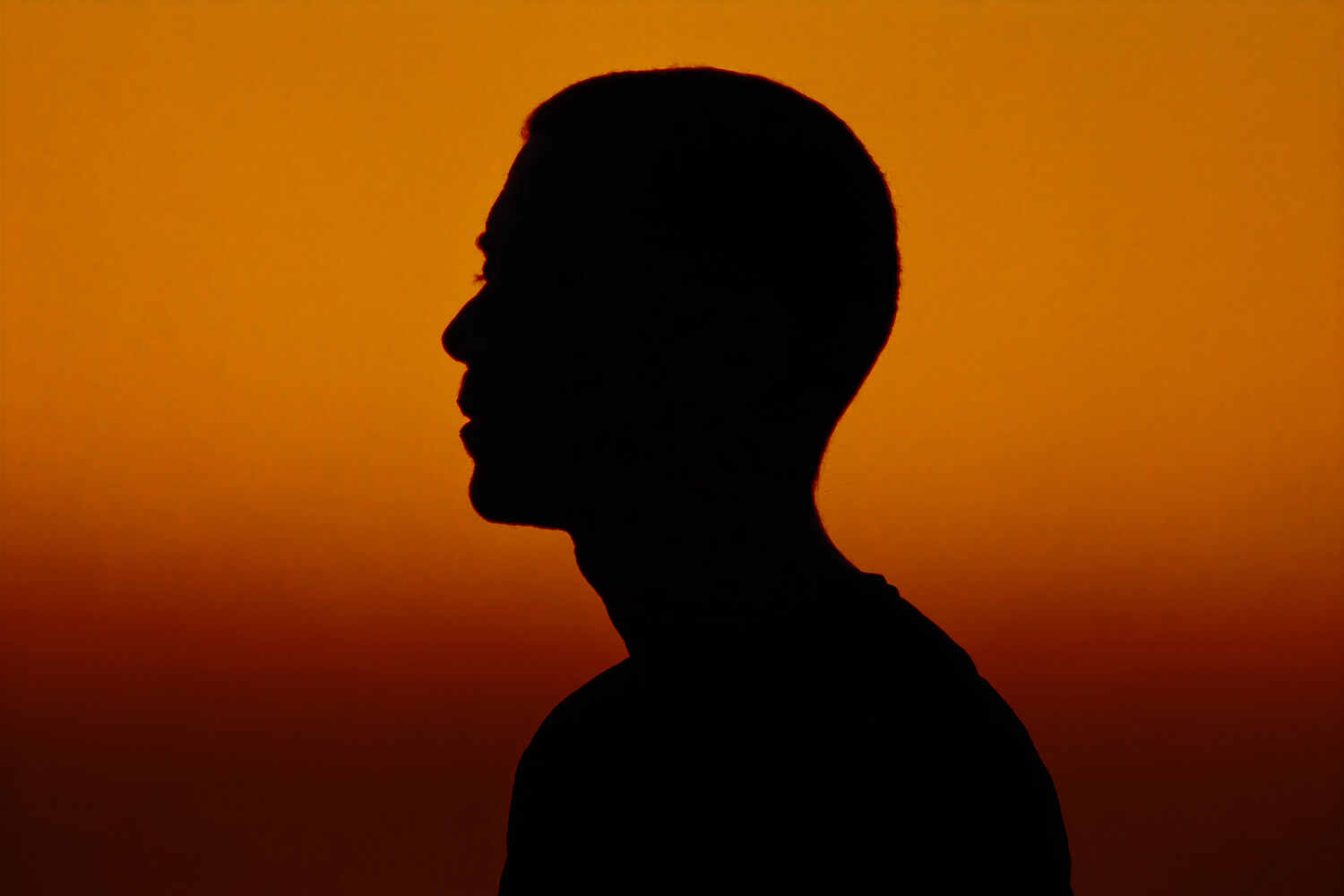 Profile silhouette of a man against an amber sunset sky